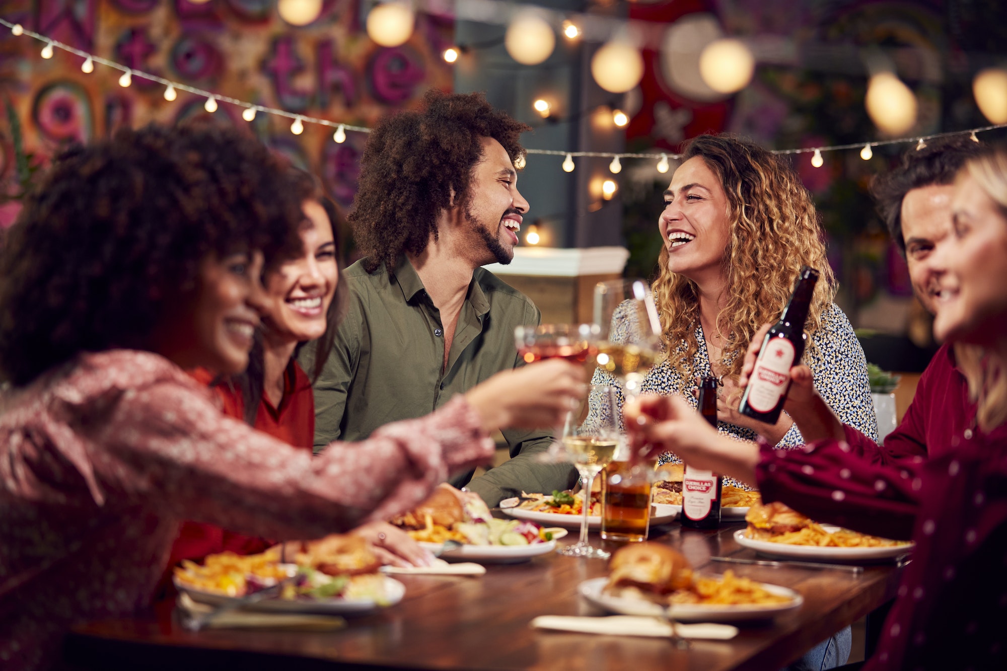 multi cultural group of friends enjoying night out eating meal and drinking in restaurant together