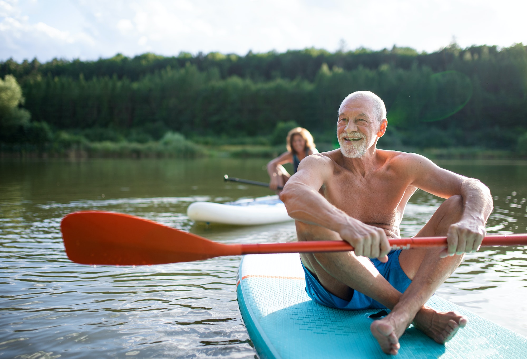 senior couple paddleboarding on lake in summer