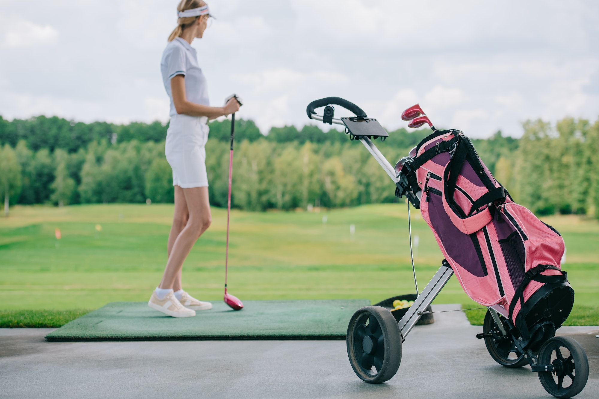 side view of woman in polo and cap with golf club standing at golf course